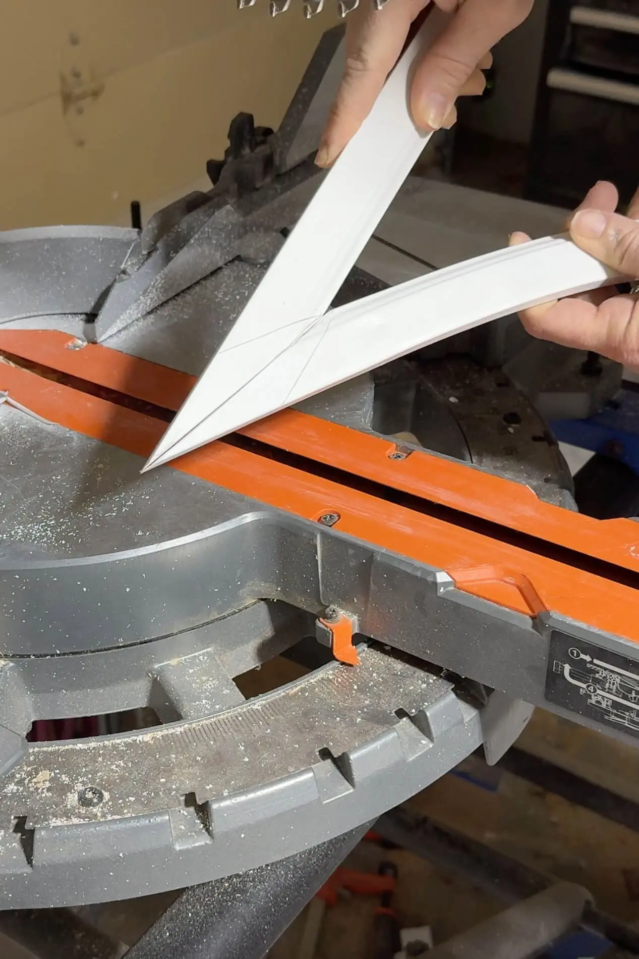 Hands holding mitered trim pieces against a miter saw, measuring precise angles for a clean finish. Sawdust adds a touch of realism to this DIY woodworking project.